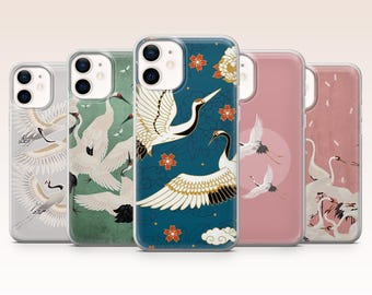 Peut inclure: Plusieurs coques de téléphone avec des motifs de grues. Les coques présentent différents coloris, notamment le bleu canard, le rose et le gris, avec des illustrations de grues blanches aux accents noirs et aux ailes dorées. Certains motifs incluent des fleurs et des nuages.