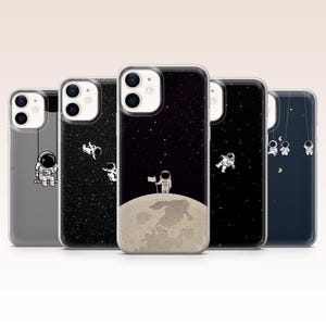 Puede incluir: Cinco fundas transparentes para teléfono con diseños de astronautas. Una funda presenta un astronauta en un columpio, otra tiene astronautas flotando en el espacio y una tercera muestra un astronauta en la luna. Las otras dos fundas tienen astronautas colgando de una cuerda y flotando en el espacio.