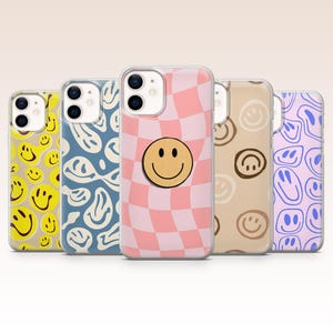 Könnte beinhalten: Eine Sammlung von fünf Handyhüllen mit verschiedenen Designs. Die Hüllen zeigen Smiley-Gesichter, Schachbrettmuster und abstrakte Designs in Gelb, Blau, Rosa, Braun und Lila. Jede Hülle hat einen transparenten Rand.