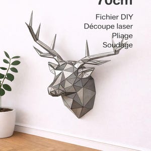 Peut inclure: Une sculpture de tête de cerf géométrique en métal, de 70 cm de haut, fixée sur un mur blanc. L'œuvre est faite de métal plié et soudé, avec du texte indiquant qu'il s'agit d'un projet de bricolage.