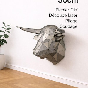 Pode incluir: Uma escultura geométrica de cabeça de touro em metal, montada numa parede branca. A escultura tem aproximadamente 50 cm de comprimento e apresenta um design facetado. O texto na imagem diz "Sculpture en métal 50cm".