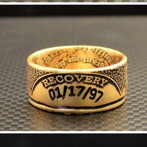 May include: Gold-toned ring with engraved text. The ring features the phrases "SELF BE TRUE SERVICE", "RECOVERY 01/17/97", and "TO THINE OWN UNITY". The ring has a textured surface and a classic design.