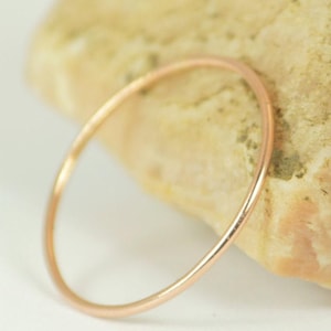 Könnte beinhalten: Ein zarter, dünner Ring aus Roségold. Der kreisförmige Ring liegt auf einer hellen Oberfläche neben einem strukturierten, hellbraunen Stein. Das schlichte Design des Rings macht ihn alltagstauglich.