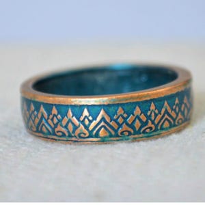 May include: A teal and gold ring with an intricate geometric pattern. The ring is displayed next to a coin with a similar design. The ring's band is teal with gold detailing, and the coin is a copper color.