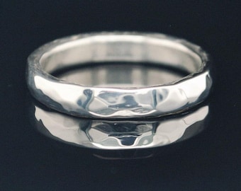 May include: A silver ring with a hammered texture. The ring is round and reflects light, creating a bright appearance. The ring is displayed on a dark, reflective surface, enhancing its shine.