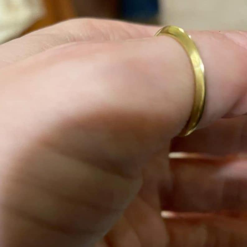 May include: A gold ring is worn on a finger. The ring has a smooth, polished surface and a simple design. The ring appears to be made of metal.