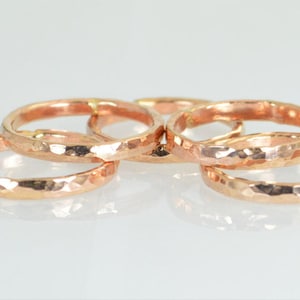 May include: Six rose gold rings with a hammered finish. The rings have a textured, faceted surface that catches the light. The rings are displayed on a white surface. The rings are made of a warm, copper-toned metal.