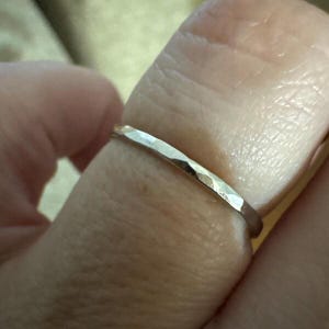 Op de afbeelding: Close-up van een gehamerde zilveren ring. De ring heeft een getextureerd oppervlak met een reeks kleine facetten, waardoor een uniek, lichtvangend effect ontstaat. De ring wordt aan een vinger gedragen en toont zijn eenvoudige maar elegante ontwerp.