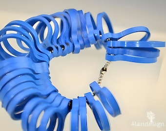 Könnte beinhalten: Ein Satz blauer Kunststoff-Ringgrößen, verbunden durch eine silberne Kette. Die Größen sind kreisförmig angeordnet, wobei jeder Ring eine andere Größe hat. Das Bild ist aus leicht erhöhter Perspektive vor weißem Hintergrund aufgenommen.