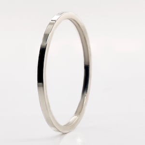 May include: A minimalist silver ring with a smooth, polished finish. The ring has a simple, elegant design, perfect for everyday wear. The band is thin and circular, with a slight twist. The ring is set against a white background.