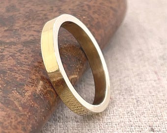 May include: A gold-colored ring with a textured band. The ring is set against a neutral background, highlighting its simple, elegant design. The ring's band has a subtle, hammered texture, adding visual interest to the piece. This ring is a piece of jewelry.