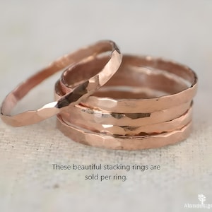 May include: A stack of hammered-finish rose gold stacking rings. The rings have a textured surface and are displayed on a light background. Text on the image reads: "These beautiful stacking rings are sold per ring."