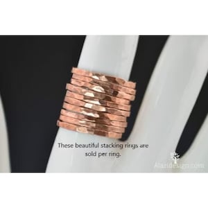 Puede incluir: Una pila de anillos de cobre martillado sobre una superficie blanca. Los anillos tienen una superficie texturizada e irregular y un color marrón rojizo cálido. Los anillos se venden individualmente. El texto de la imagen dice: "Estos hermosos anillos apilables se venden por anillo."