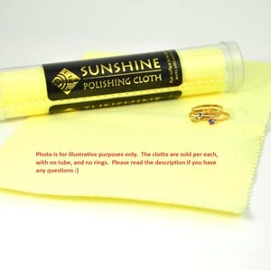 May include: A yellow polishing cloth with a tube of Sunshine Polishing Cloth and two gold rings with gemstones. The text on the tube reads "SUNSHINE POLISHING CLOTH". The image also includes the text: "Photo is for illustrative purposes only."