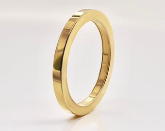 May include: A gold-colored ring with a flat, rectangular band. The ring has a smooth, polished surface and a simple, modern design. The ring is shown against a white background.