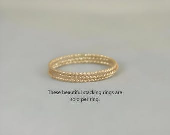 May include: A set of three gold-colored stacking rings. The rings have a textured, beaded design. The rings are displayed on a light gray background. The text in the image says "These beautiful stacking rings are sold per ring."