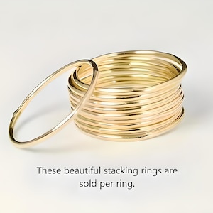 Puede incluir: Un conjunto de anillos apilables dorados, con un anillo ligeramente separado. Los anillos son redondos y parecen ser de metal. El texto de la imagen dice: "These beautiful stacking rings are sold per ring."