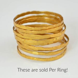 May include: A stack of gold-colored rings with a hammered texture. The rings are stacked on top of each other, with the text "These are sold Per Ring!" at the bottom of the image. The rings have a slightly irregular shape.