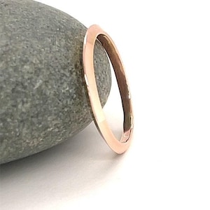 Puede incluir: Un anillo de oro rosa con un acabado liso y pulido. El anillo se presenta sobre una piedra gris y un fondo blanco. El diseño del anillo es simple y elegante, adecuado para el uso diario o ocasiones especiales.