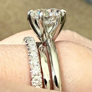 Op de afbeelding: Een close-up van een diamanten verlovingsring met een grote, rond geslepen middensteen. De ring is gezet in een zilveren band met een zes-klauwzetting. Een kleinere band met pav&eacute;-diamanten ligt ernaast.