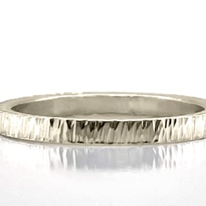 Op de afbeelding: Een zilveren ring met een getextureerd, op schors lijkend oppervlak. De band is een eenvoudig, dun ontwerp, ideaal voor dagelijks gebruik. Het oppervlak van de ring heeft een ruwe, ongelijke textuur.
