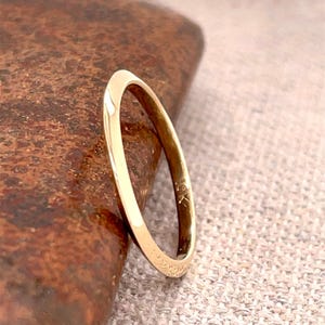 Op de afbeelding: Een gouden ring met een gladde, afgeronde band. De ring is geplaatst tegen een getextureerd, bruin oppervlak. De ring lijkt gemaakt te zijn van 10K goud.