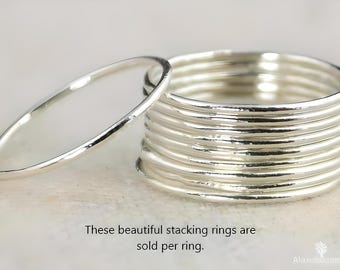 Op de afbeelding: Een stapel zilveren stapelringen met één ring ernaast. De ringen zijn glad en glanzend. Ze liggen op een lichtgekleurd oppervlak. De tekst in de afbeelding luidt: "Deze prachtige stapelringen worden per ring verkocht."