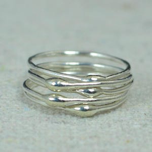 Könnte beinhalten: Ein Stapel silberner Ringe mit einem einzigartigen Design. Jeder Ring weist eine Reihe kleiner, abgerundeter Perlen auf seiner Oberfläche auf, die einen strukturierten und auffälligen Look erzeugen. Die Ringe sind übereinander gestapelt und zeigen ihre komplizierten Details.