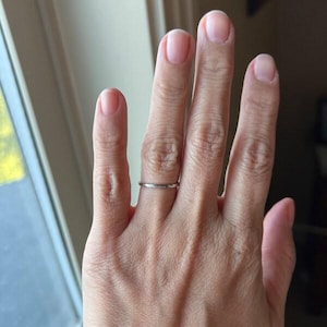 Op de afbeelding: Een dunne, zilveren ring wordt aan een vinger gedragen. De ring lijkt een eenvoudige band te zijn, mogelijk een trouwring of een minimalistisch sieraad. Het ontwerp van de ring is ingetogen en elegant.