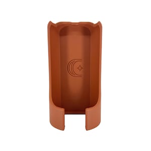 May include: A terracotta-colored, rectangular holder with a curved top and a crescent moon and star design. The holder has a hollow interior and two small rectangular cutouts at the base.