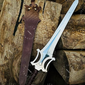 May include: A silver sword with a double-edged blade and a decorative hilt rests beside a brown leather sheath. The sheath is stitched and has a strap for carrying. The sword and sheath are displayed on a background of stacked wooden logs.