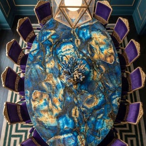 May include: An oval dining table with a polished blue and gold stone surface featuring intricate veining, surrounded by twelve purple velvet chairs with ornate gold frames. A large geometric gold pendant light hangs above the table.