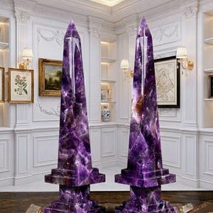 May include: Two tall, pointed obelisks carved from deep purple amethyst crystal. Each piece features a faceted, multi-sided structure tapering to a sharp apex, resting on a square, tiered base with visible natural crystalline inclusions and veins.