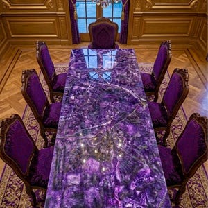 May include: A rectangular dining table with a polished purple amethyst gemstone surface, surrounded by eight high-backed chairs upholstered in deep purple velvet fabric, positioned on a patterned purple and gold area rug in a room.