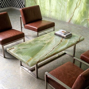 May include: A rectangular coffee table with a polished green onyx stone top and a silver-toned metal frame, accompanied by three armless chairs featuring brown leather upholstery and matching silver-toned metal frames.