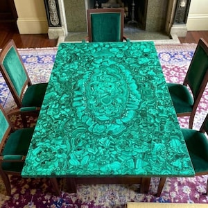 Può includere: Un tavolo da pranzo rettangolare con una superficie dal vivace motivo a malachite verde, accompagnato da cinque sedie in legno con rivestimento in velluto verde scuro su sedute e schienali, disposte attorno al tavolo.