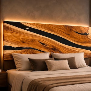 May include: A rectangular headboard featuring natural wood grain with a prominent black resin river inlay running diagonally across the surface. The headboard is backlit with warm LED lighting and positioned above a bed with neutral-toned pillows.