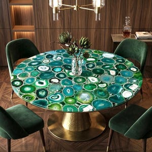 Puede incluir: Una mesa de comedor redonda con una tapa de piedra de ágata verde, sostenida por una base dorada. Cuatro sillas de terciopelo verde rodean la mesa. Un jarrón de vegetación se encuentra sobre la mesa. La habitación tiene paneles de madera y una lámpara de araña.