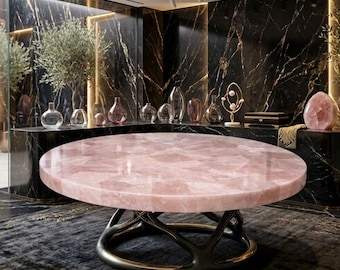 May include: A large, round table with a pink, mosaic-like top. The table has a dark, ornate base with a gold-colored ring. The background features a black marble wall with decorative vases and a large rose quartz crystal.
