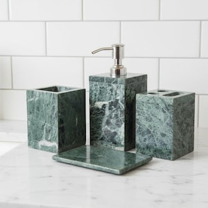 Può includere: Un set da bagno in marmo verde composto da quattro pezzi. Il set include un dosatore di sapone con pompa argentata, un portaspazzolino, un bicchiere e un portasapone. Il marmo presenta venature naturali.
