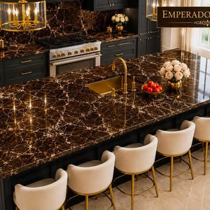 Puede incluir: Una isla de cocina con encimera de mármol Emperador marrón oscuro con vetas blancas, fregadero y grifo dorados, y cinco taburetes de bar tapizados en color crema con patas de metal dorado, frente a gabinetes de color oscuro.
