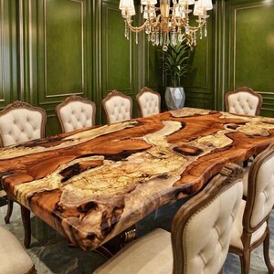 May include: A large, rectangular dining table with a unique wood grain pattern in shades of brown, tan, and cream. The table is surrounded by several ornate chairs with cream-colored upholstery and wooden frames. A gold chandelier hangs above.