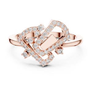 May include: Rose gold ring with a unique, geometric design. The ring features a series of interconnected shapes, embellished with numerous small, sparkling clear stones. The band is a simple, polished rose gold.