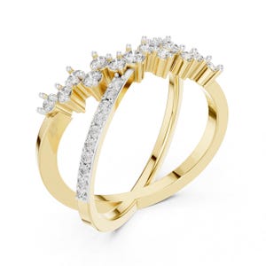 K&ouml;nnte beinhalten: Ein goldfarbener Ring mit einem Doppelband-Design. Ein Band ist mit kleinen, klaren Edelsteinen besetzt, das andere mit gr&ouml;&szlig;eren, klaren Edelsteinen. Der Ring ist vor einem wei&szlig;en Hintergrund abgebildet.