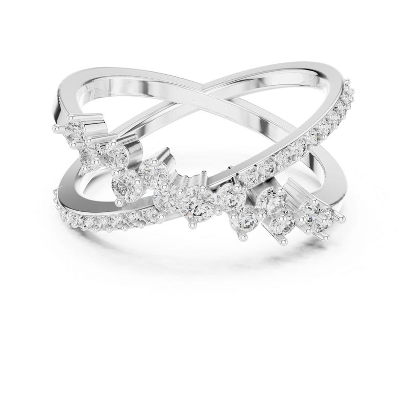 K&ouml;nnte beinhalten: Ein silberfarbener Ring mit einem Kreuzmuster. Der Ring ist mit zahlreichen kleinen, klaren Edelsteinen entlang des Bandes und in einem bl&uuml;tenartigen Muster besetzt. Der Ring ist vor einem wei&szlig;en Hintergrund platziert.