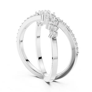 K&ouml;nnte beinhalten: Ein silberner Ring mit einem einzigartigen Design. Der Ring hat drei B&auml;nder, wobei zwei die Hauptstruktur bilden und ein drittes, gebogenes Band mit kleinen, klaren Steinen besetzt ist. Oben ist eine Ansammlung gr&ouml;&szlig;erer Steine gesetzt.