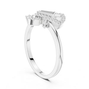 May include: A silver ring with a unique design, featuring a cluster of small, sparkling stones around a larger, rectangular stone. The ring's band is smooth and polished, creating a modern and elegant look.