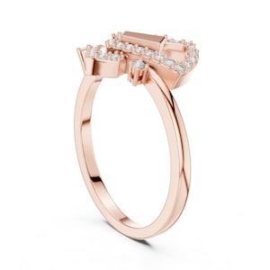 May include: Rose gold ring featuring a cluster of small, round, and baguette-cut clear gemstones. The ring's band is a smooth, polished rose gold. The gemstones are set in a decorative pattern, creating a sparkling effect. The ring is designed with a modern aesthetic.