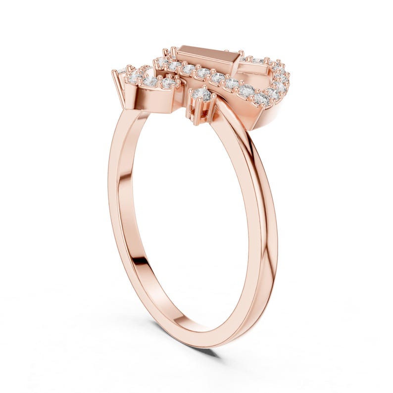 May include: Rose gold ring featuring a cluster of small, round, and baguette-cut clear gemstones. The ring's band is a smooth, polished rose gold. The gemstones are set in a decorative pattern, creating a sparkling effect. The ring is designed with a modern aesthetic.