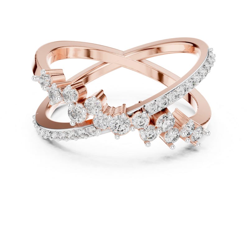 K&ouml;nnte beinhalten: Ring in Ros&eacute;gold-Optik mit einem Kreuzmuster. Ein Band ist mit kleinen, klaren Kristallen besetzt, w&auml;hrend das andere schlicht ist. An dem mit Kristallen besetzten Band sind Gruppen gr&ouml;&szlig;erer, klarer Kristalle angeordnet.